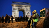 (Files) French farmers are seen sitting on a bale of hay as policemen secure the area in front of the Arc de Triomphe near the Champs-Elysees Avenue during a protest by the French farmers' union in Paris on March 1, 2024. (Photo by Thomas Samson / AFP)