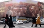 Women walk in front of a banner covering the facade of a building in Tehran, hours before his funeral in Beirut on February 23, 2025. (Photo by Atta Kenare / AFP)
