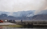 This picture taken on March 3, 2025 shows people watching a wildfire which approaches a village from the fishing port of Ofunato city in Iwate prefecture. (Photo by JIJI PRESS / AFP) 