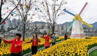 Women dance for a video next to flowers and a windmill by Jialing river in Yuzhong District in Chongqing in southwestern China on March 6, 2025. (Photo by Hector RETAMAL / AFP)