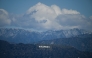 Snow dusted mountains stand on the skyline behind a view of the Hollywood sign following rain storms, as seen from the Kenneth Hahn State Recreation Area, in Los Angeles, California on March 7, 2025. (Photo by Patrick T. Fallon / AFP)
