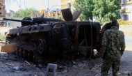 This picture shows a fighter in front of a burnt military vehicle, in Khartoum North, on March 17, 2025. Nearly two years of war between the army and the paramilitary Rapid Support Forces (RSF) have left large swathes of Sudan's capital unrecognisable. (Photo by Ebrahim Hamid / AFP)
