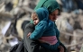 A Palestinian woman carries a baby as families leave the eastern sector of the Gaza Strip on the border with Israel following Israeli airstrikes that targeted northern and other parts of Gaza in the early hours of March 18, 2025. Gaza's civil defence agency said the death toll from a massive Israeli campaign launched throughout the Palestinian territory rose to more than 400 people, including children. Photo by Bashar TALEB / AFP.