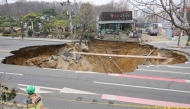 Rescue workers walk past a sinkhole outside a plant shop on a road in Seoul on March 25, 2025. (Photo by Anthony Wallace / AFP)