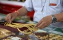 An employee handles gold jewelry for customers at Hua Seng Heng gold traders in Chinatown in Bangkok on April 9, 2025. (Photo by Lillian SUWANRUMPHA / AFP)
