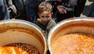 A Palestinian child waits to receive his portion of food a distribution point at the Nuseirat refugee camp in the central Gaza Strip on April 12, 2025. Photo by Eyad BABA / AFP.