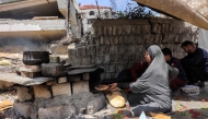 A woman bakes pita bread loaves in an oven by a tent in Gaza City on April 21, 2025. (Photo by Omar AL-QATTAA / AFP)