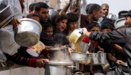 People queue with pots to receive charity meals from a kitchen in Beit Lahia in the northern Gaza Strip on April 24, 2025. (Photo by Bashar Taleb / AFP)