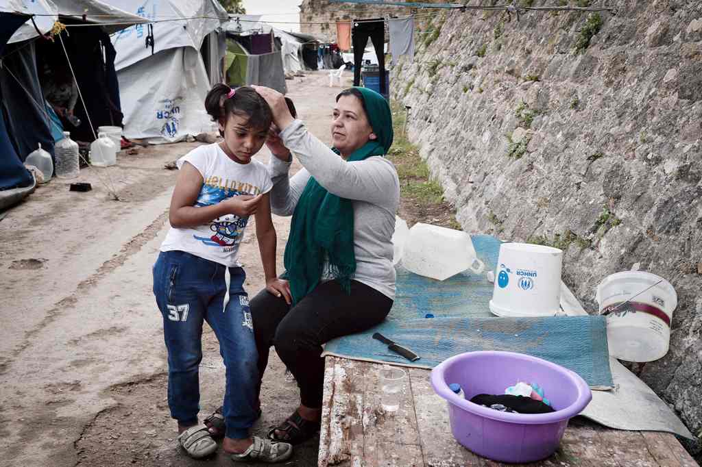 A Syrian Kurd mother combs Roza's hair, as she prepares to go to a volunteer-run school in a refugee camp on the island of Chios on October 13, 2016.  AFP / LOUISA GOULIAMAKI