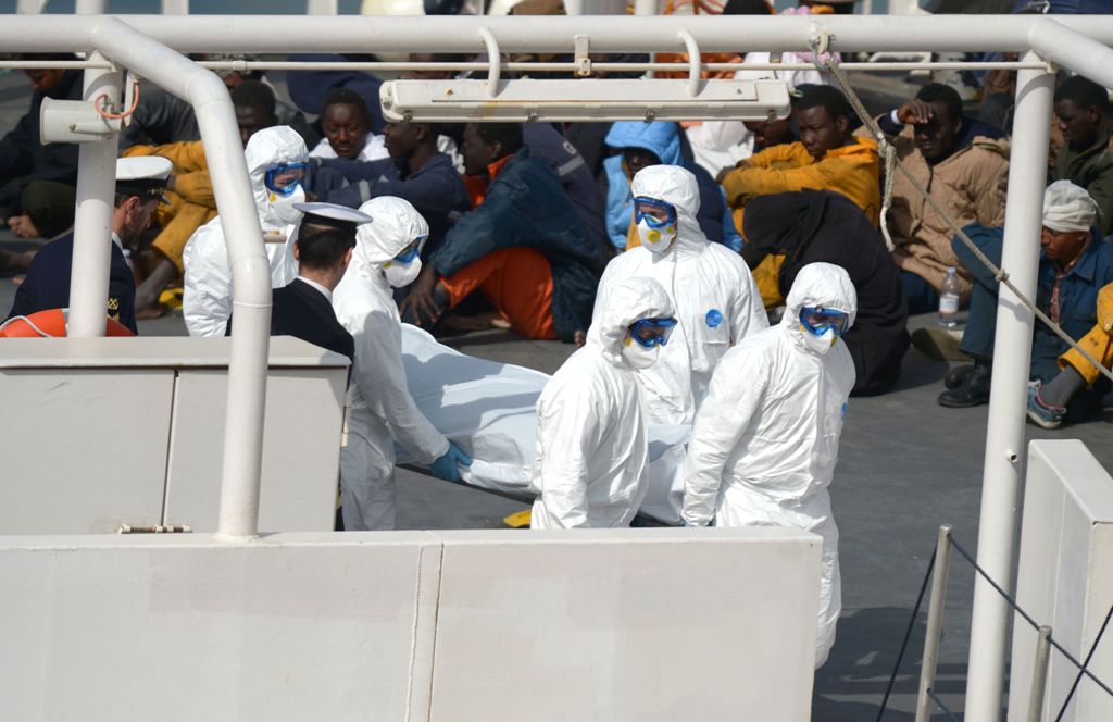 (FILES) This file photo taken on April 20, 2015 shows rescued migrants watching as the body of a person who died after a fishing boat carrying migrants capsized off the Libyan coast, is brought ashore along with 23 others retreived by the Italian Coast Gu