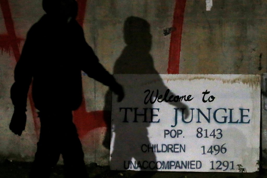 The shadow of a migrant falls on a sign with the population of 