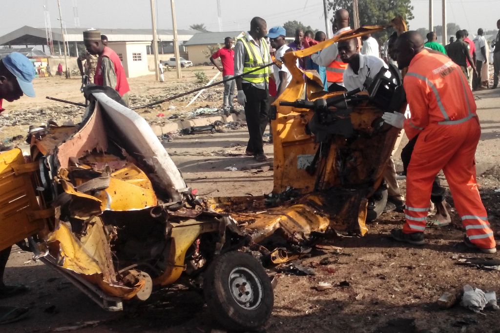 Emergency personnel stand near the wreacked remains of a vehicle ripped apart following two suicide bombings in Nigeria's northeast city of Maiduguri on October 29, 2016 where at least nine people and scores of others were injured.  / AFP / JOSHOUA OMIRIN