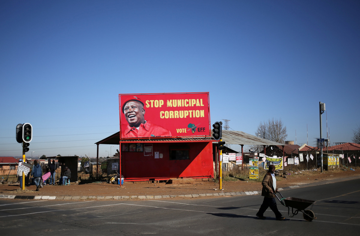 A man pushes a wheelbarrow past a billboard of the Economic Freedom Fighters which is led by Julius Malema in Soweto, South Africa, August 5, 2016.  (REUTERS / Siphiwe Sibeko) 