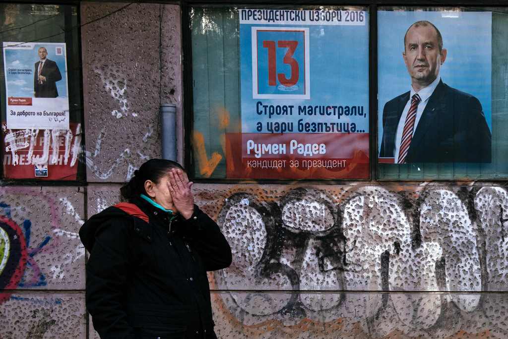 A street vendor hides her face as she sells clothes in front of electoral posters of former Bulgarian airforce chief Rumen Radev, candidate of the opposition Socialists, in Sofia on November 11, 2016. AFP / DIMITAR DILKOFF