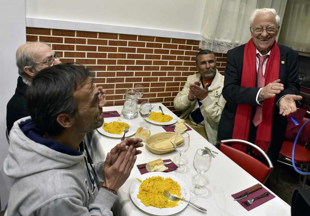 Father Angel Garcia Rodriguez (R) claps beside homeless people eating a free dinner at the Robin Hood restaurant in Madrid on December 1, 2016. AFP / GERARD JULIEN
