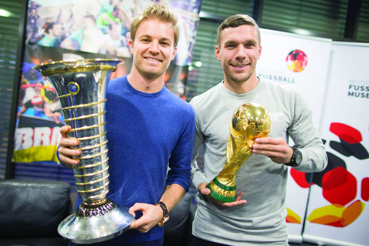 Formula One World Champion Nico Rosberg (left) raises the trophy next to former German player Lukas Podolski with the football World Cup trophy in Cologne, Germany on Wednesday.