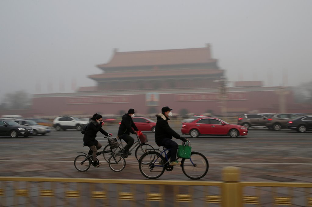 People wearing masks cycle past Tiananmen Gate during the smog after a red alert was issued for heavy air pollution in Beijing, China, December 20, 2016. REUTERS/Jason Lee
