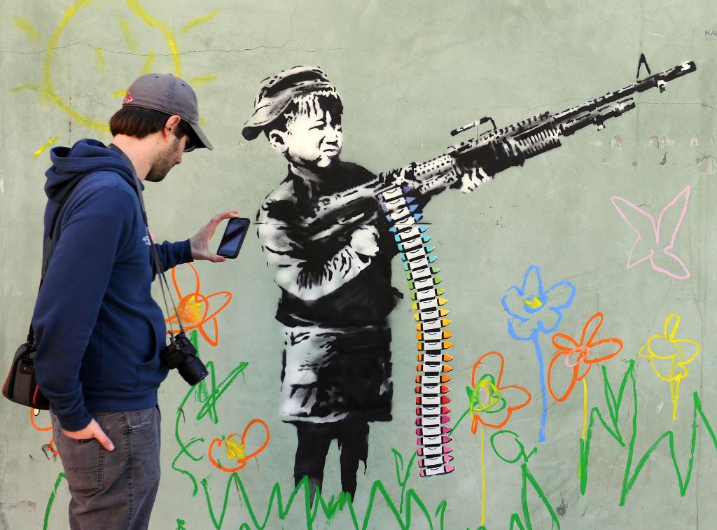 (FILES) This file photo taken on February 17, 2011 shows a graffito attributed to secretive British artist Banksy, depicting a child wielding a machine gun, in black and white, surrounded by colored flowers, in Westwood, California. AFP / GABRIEL BOUYS