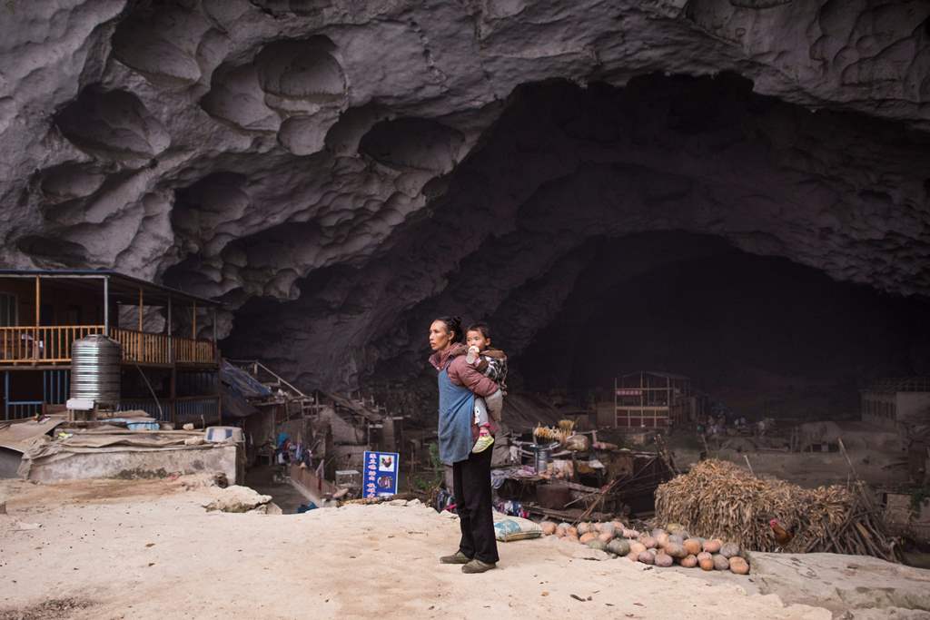 This photo taken on November 6, 2016 shows a woman holding a baby on her back in the village of Zhongdong, where a group of 18 families live inside an enormous natural cave. AFP / FRED DUFOUR
