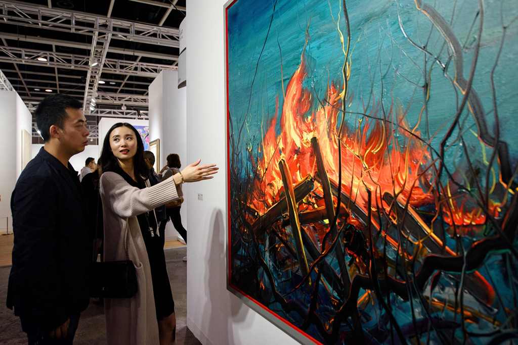 In this picture taken on March 22, 2017, Chinese investment banker Huang Xiaoshuai, 26, and his wife Wei Mengyuan chat in front of their newly acquired painting 'Fire' by Chinese artist Zeng Fangzhi, during an interview with AFP at Art Basel in Hong Kong.