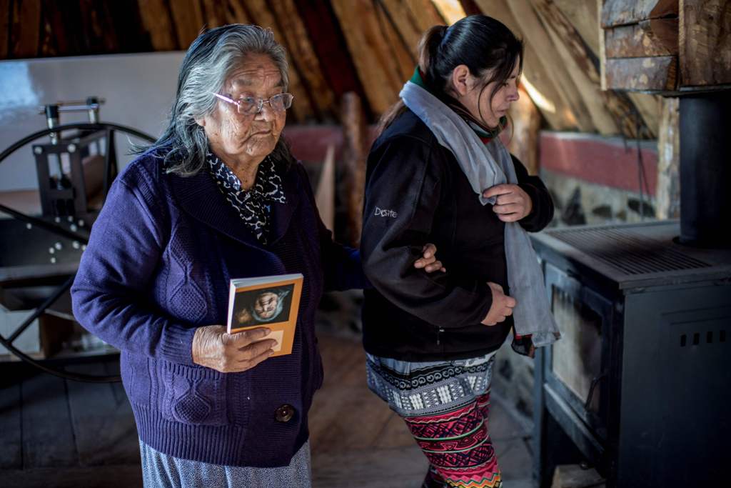 Holding a copy of her book, Cristina Calderon (L), 89, the last native speaker of the Yagan language, walks with her granddaughter Claudia Gonzalez in the local community center in Puerto Williams, southern Chile, on April 23, 2017. AFP / Martin BERNETTI
