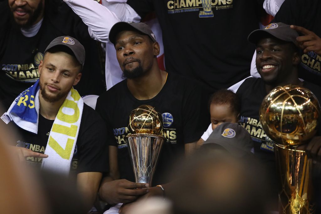 Stephen Curry #30, Kevin Durant #35 with the Bill Russell NBA Finals Most Valuable Player Award and Draymond Green #23 (holding the Larry O'Brien Championship Trophy) of the Golden State Warriors celebrate after defeating the Cleveland Cavaliers 129-120 i