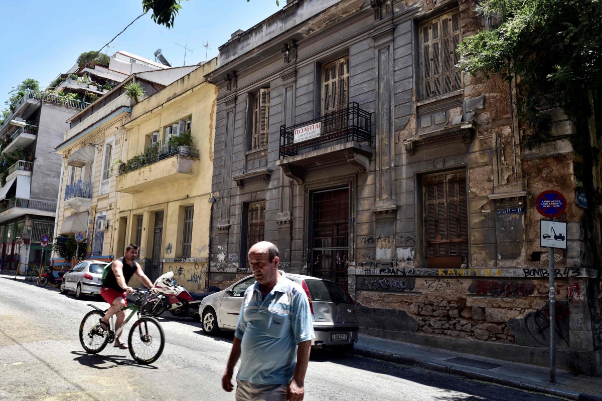 People pass a neoclassical building for sale in one of the oldest districts of Athens on July 7, 2017. AFP / Louisa Gouliamaki