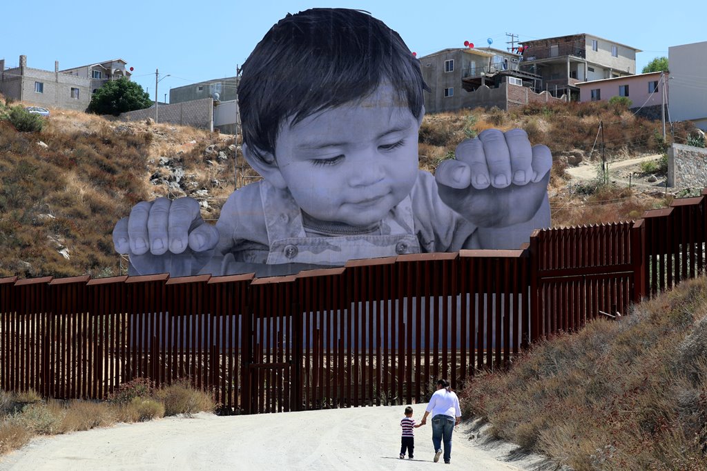 A small boy walks with his mother in front of French artist JR's image of an inquisitive baby looking into the United States over the U.S.- Mexico border wall towards Tecate, California, U.S., September 15, 2017. REUTERS/Mike Blake 
