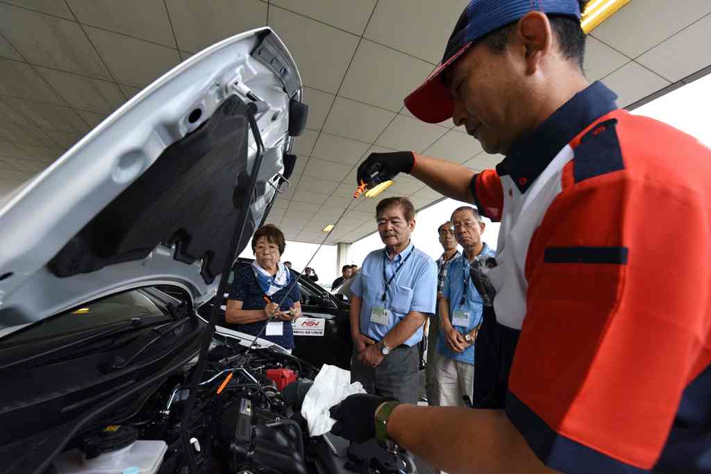 This picture taken on July 23, 2017 shows an instructor (R) using a dipstick to check engine oil levels during a lesson on car maintenance at a driving school for senior citizens, managed by the Japan Automobile Federation (JAF), in Kanuma, Tochigi prefec