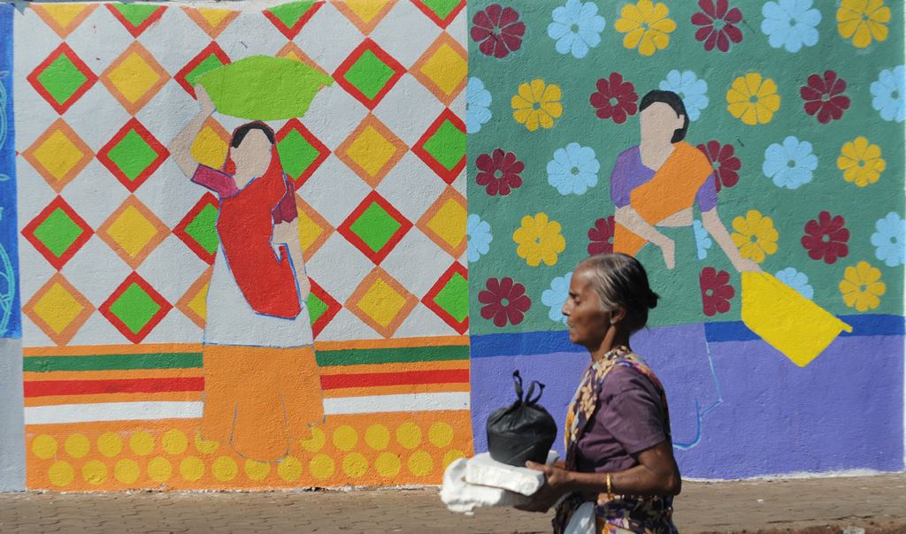 This photo taken on November 9, 2017 shows a fisherwoman walking past a wall painting of the St+art Festival at Sassoon Dock, one of the oldest fishing docks in Mumbai. AFP / INDRANIL MUKHERJEE 