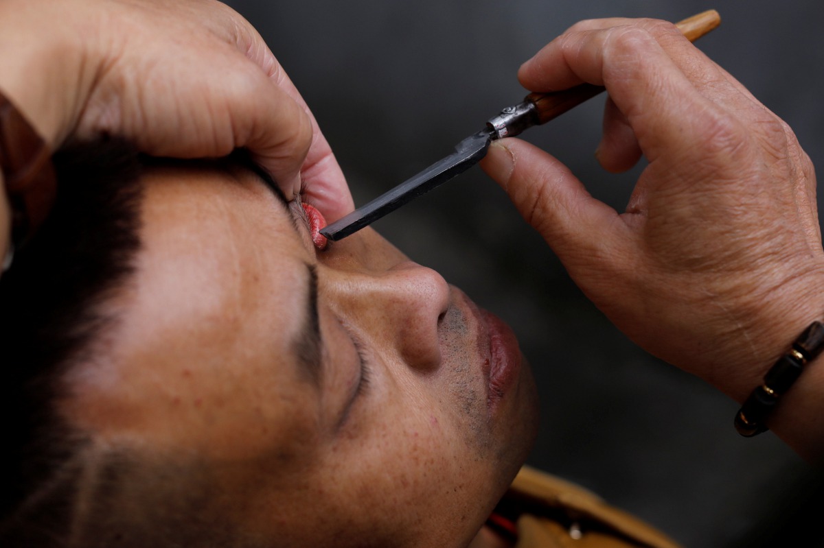 A file photo of Xiong Gaowu, a 62-year old street barber cleans his customer eye using the straight razor in Chengdu, Sichuan province, China. REUTERS/Tyrone Siu