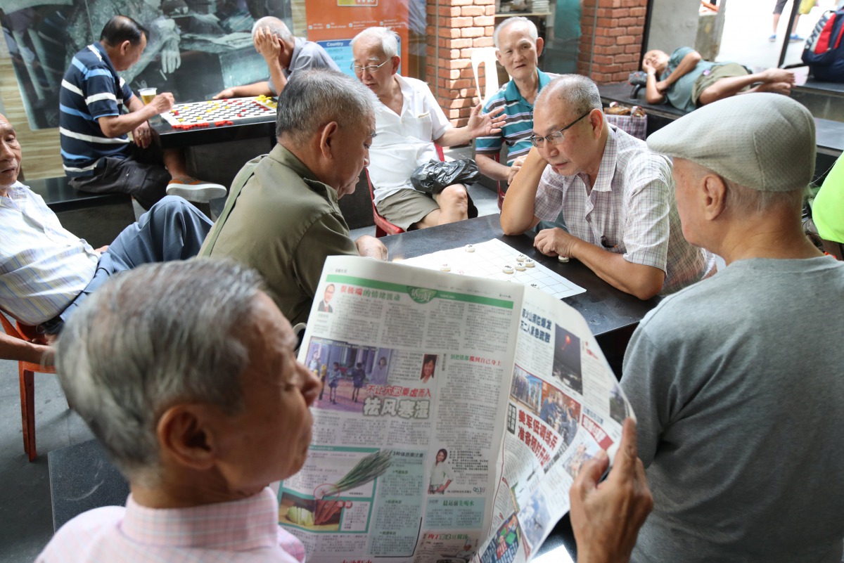 A man reads a newspaper as others play checkers in Singapore January 16, 2018. Reuters/Calvin Wong