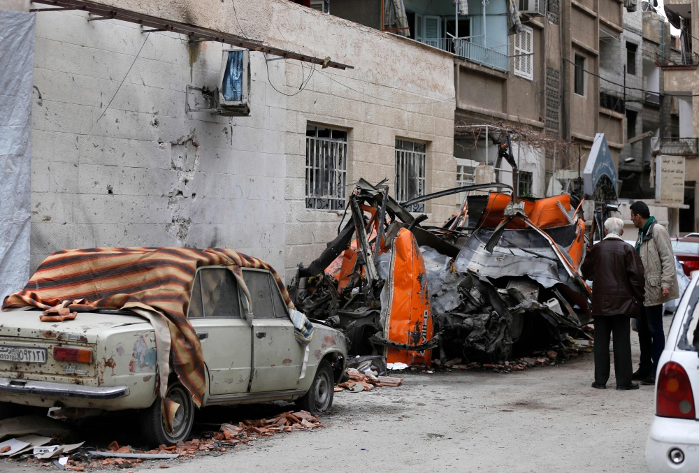 Syrians look at damaged vehicles in a street that was reportedly struck by mortar shrapnel from rebel bombardment the previous day in Jaramana, southeast of the Syrian capital Damascus, on February 12, 2018. / AFP / LOUAI BESHARA
