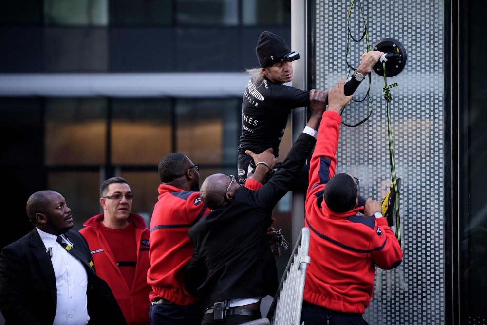 Alain Robert, the French urban climber dubbed Spiderman, is grabbed by security guards preventing him to climb a building hosting the headquarters of French energy giant Engie at La Defense business area, on March in Paris on March 14, 2018. AFP / PHILIPP