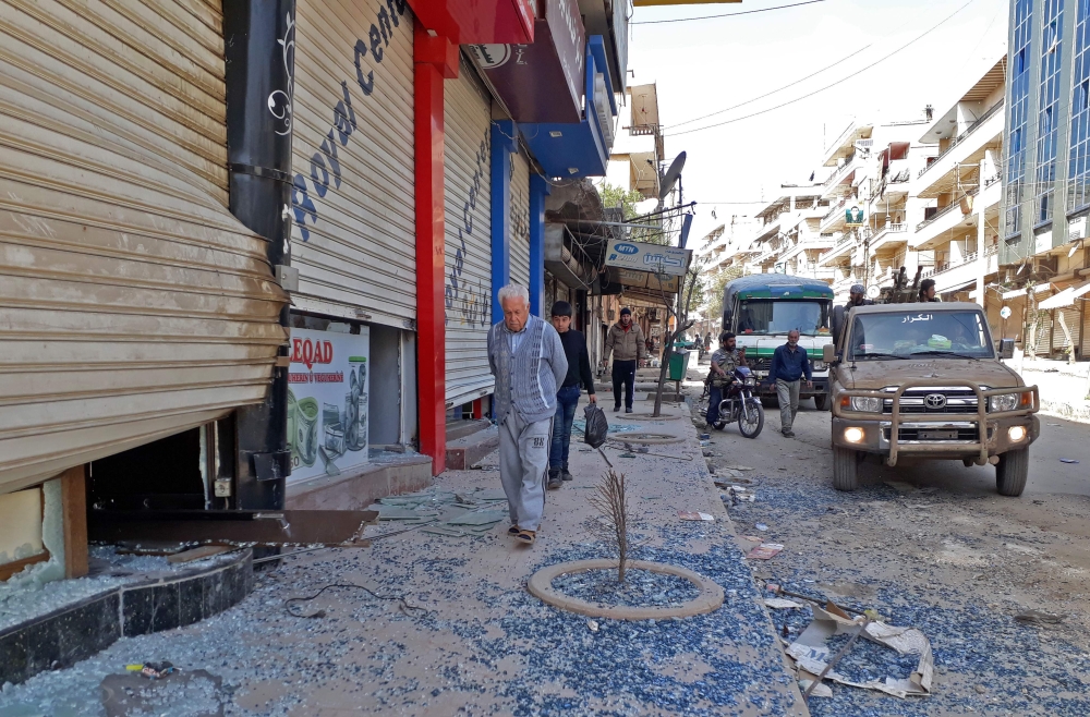 A picture taken on March 19, 2018, shows a man walking near broken glass next to Turkish-backed Syrian fighters in the seized Kurdish-majority city of Afrin.  AFP 
