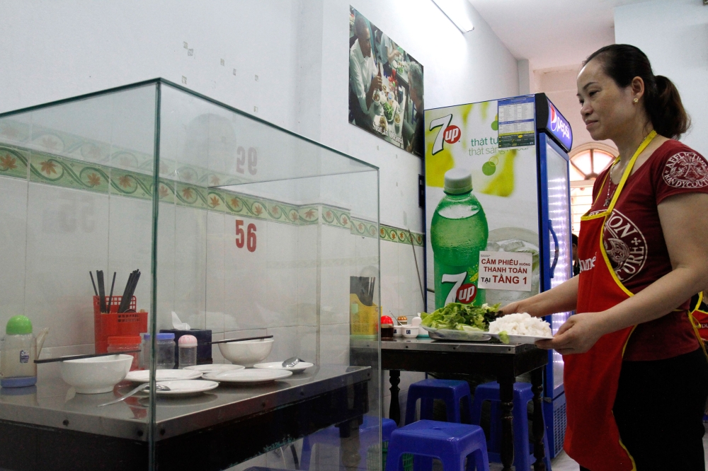 In this photograph taken on March 20, 2018, a waitress carries dishes to customers next to the glass-encased table where former US President Barack Obama sat at for a meal with chef Anthony Bourdain at Bun Cha Huong Lien restaurant, now dubbed 