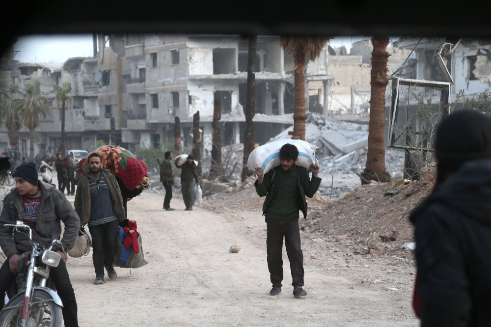 Syrian people carry their belongings as they walk down a destroyed street as they prepare to evacuate one of the few remaining rebel-held pockets in Arbin, in Eastern Ghouta, on the outskirts of the Syrian capital Damascus, on March 24, 2018.  AFP / ABDUL