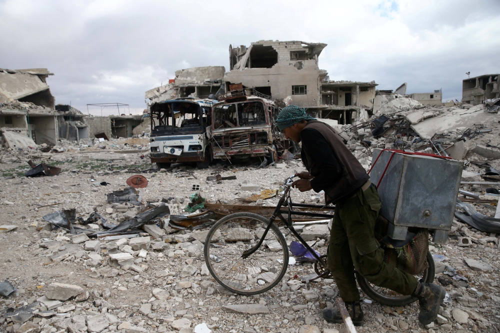 A man walks with his bicycle at a damaged site in the besieged town of Douma, Eastern Ghouta, in Damascus, Syria March 30, 2018. REUTERS/Bassam Khabieh
