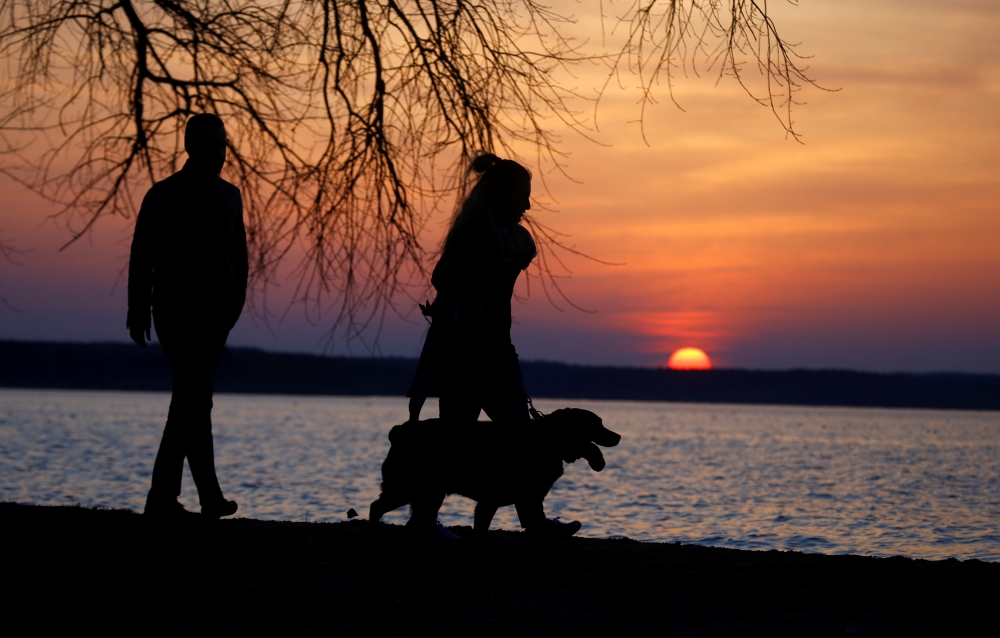 People with a dog enjoy sunset at a lake on the outskirts of Minsk, Belarus April 10, 2018. Reuters/Vasily Fedosenko