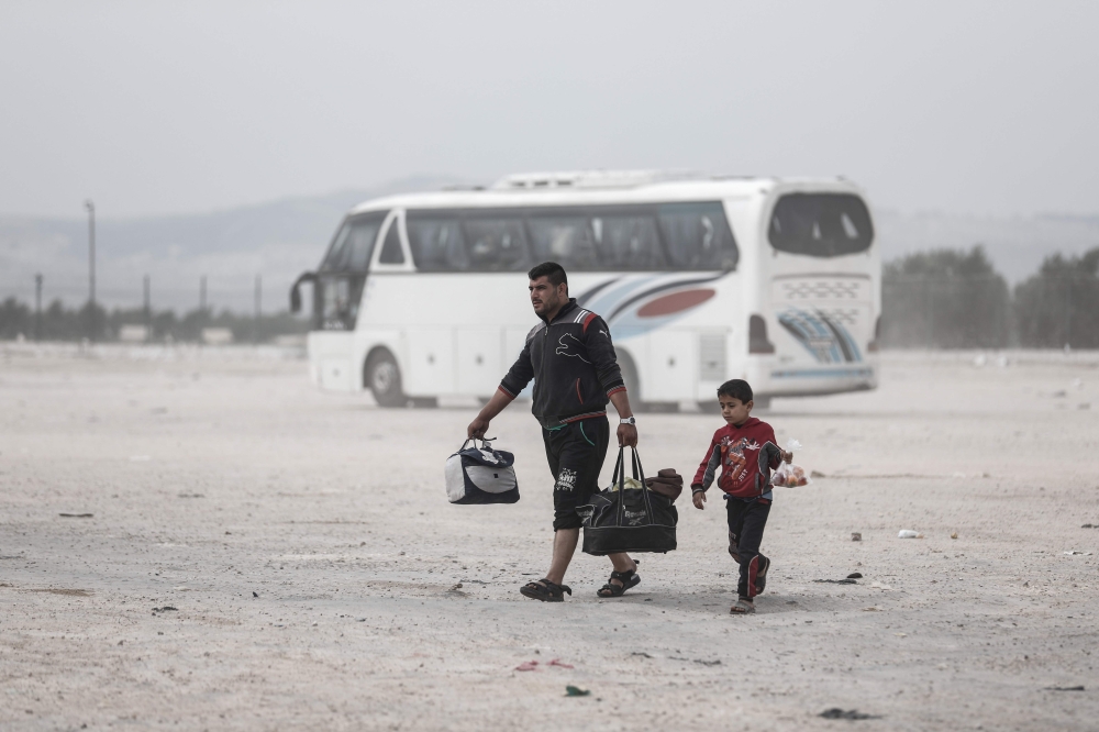 Members of a Syrian family evacuated from the town of Dumayr, east of the capital Damascus, carry their belongings as they walk away after disembarking from their bus in the city of Azaz in the northern countryside of Aleppo on April 20, 2018. AFP / Samee