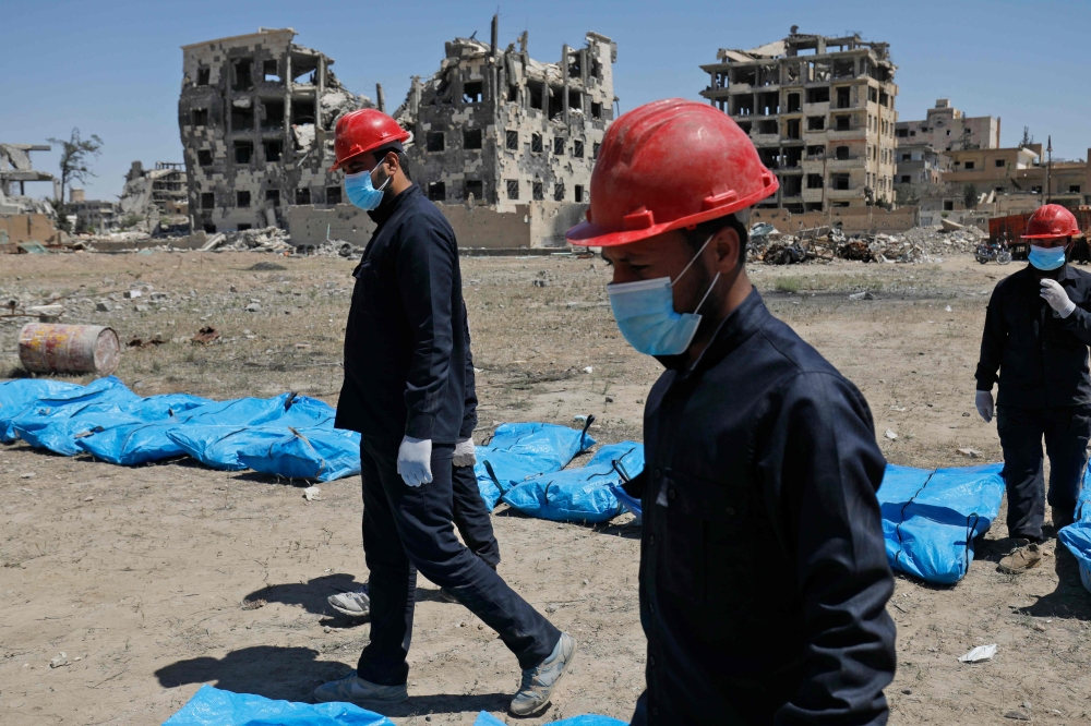 Syrians recovering bodies that have been found in a mass grave in the former Islamic State group stronghold of Raqa in Syria.  AFP / Delil souleiman
