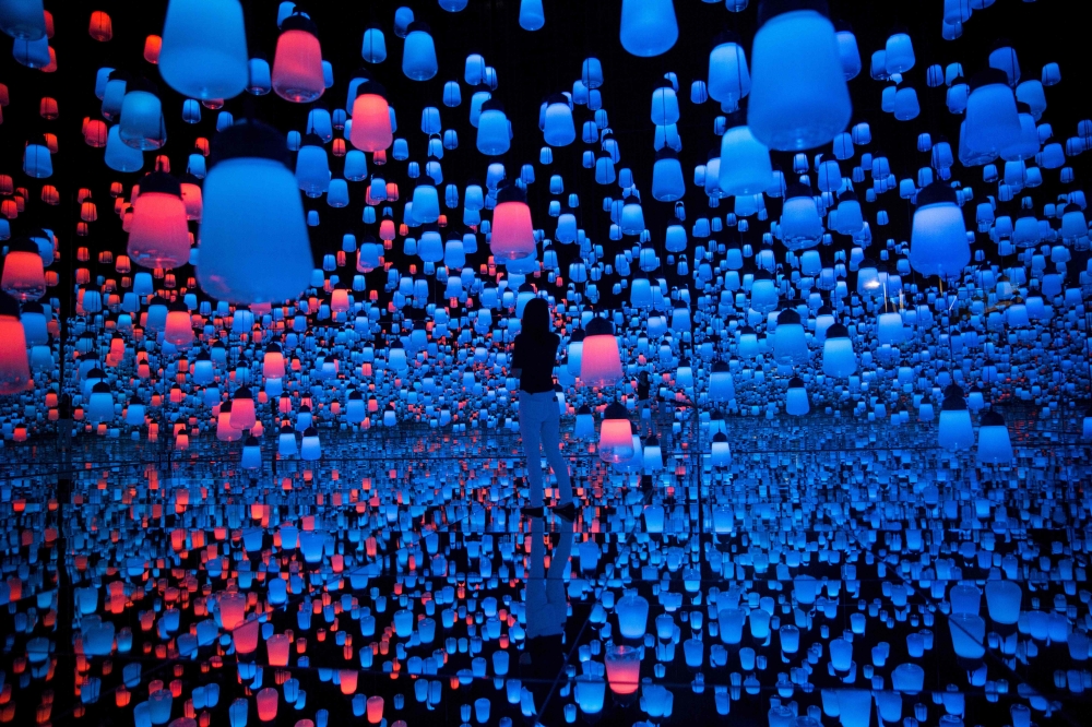 In this picture taken on May 1, 2018 a Japanese member of Teamlab collective walks and poses in a digital installation room with hanging lamps, that illuminate as the visitor nears and the light moving from one lamp to another around the room, at Mori Bui