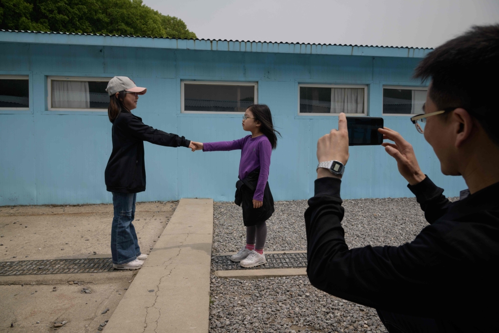 Visitors stand before a mock military demarcation line as they pose for photos at a replica of the DMZ border truce village of Panmunjom, built as a film set, near Namyangju, east of Seoul on May 5, 2018. AFP / Ed Jones