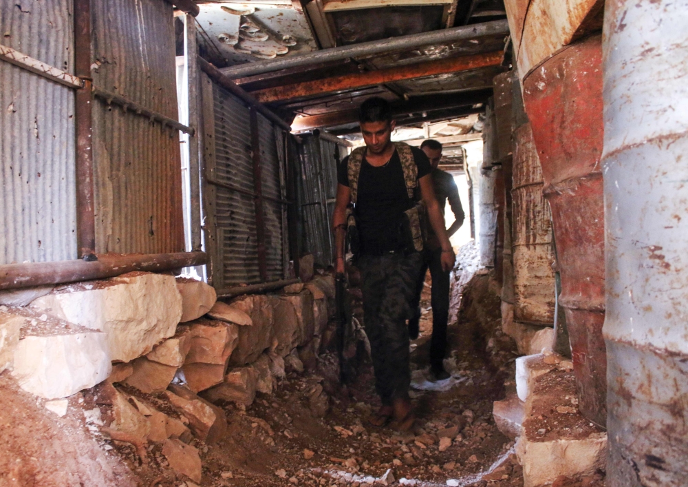 Moawiya Sayasina, the Syrian activist who started scribbling anti-Assad slogans in 2011, walks through a trench carrying a Kalashnikov assault rifle at a fortified position near the frontline in a rebel-held neighbourhood in the southern Syrian city of Da