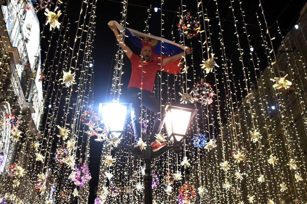 A Russia's national football team fan stands on a lamp post as he celebrates their team's victory outside the Kremlin after the Russia 2018 World Cup Group A football match between Russia and Egypt at the Saint Petersburg Stadium in Saint Petersburg on Ju