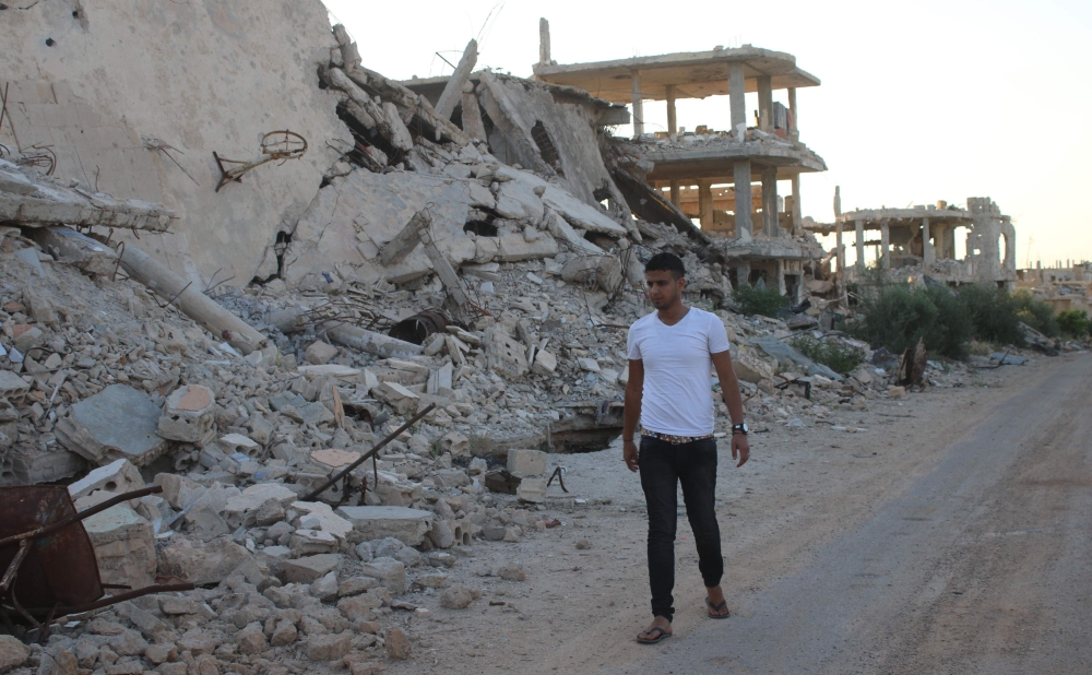 FILE PHOTO. Moawiya Sayasina, the Syrian activist who started scribbling anti-Assad slogans in 2011, walks past the rubble of destroyed buildings in a rebel-held neighbourhood in the southern Syrian city of Daraa on June 5, 2018. AFP / Mohamad ABAZEED
