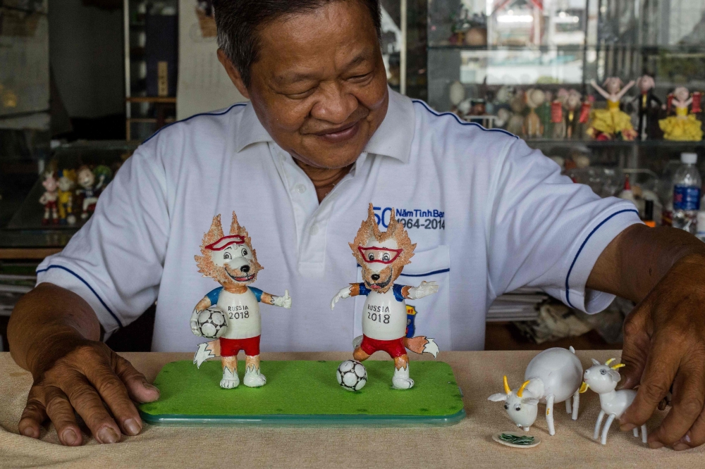 This picture taken on June 20, 2018 shows retired Vietnamese English teacher Nguyen Thanh Tam displaying two finished models of Zabivaka (L), the 2018 Russian World Cup mascot, made from eggshells, at his home in Ho Chi Minh City.  / AFP / Thanh NGUYEN