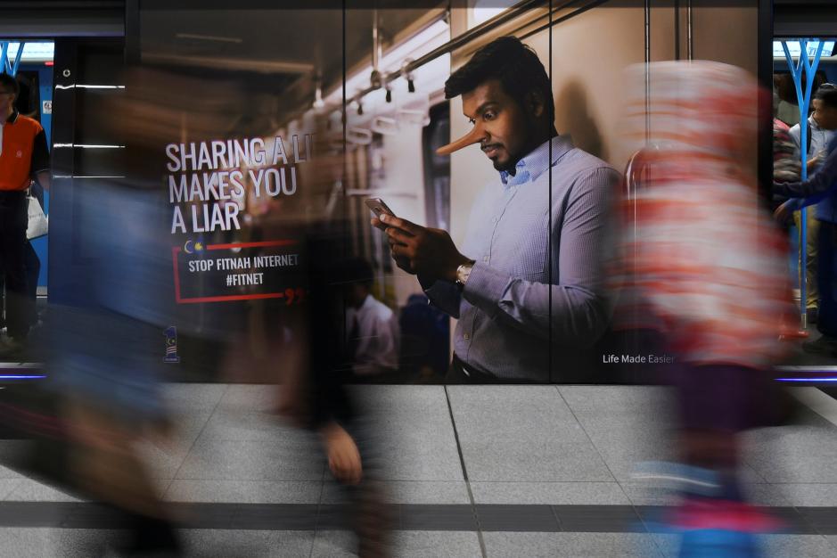 Commuters walk past an advertisement discouraging the dissemination of fake news at a train station in Kuala Lumpur, Malaysia March 28, 2018. Reuters/Stringer