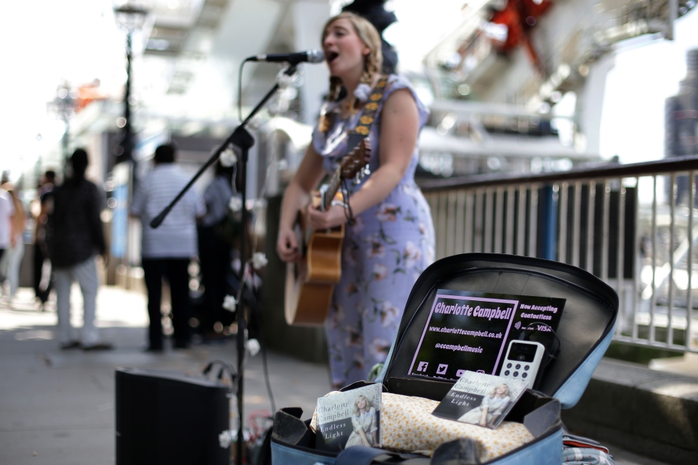 Busker Charlotte Campbell, who uses a contactless card reader for donations in addition to cash, performs near the London Eye in central London on September 1, 2018. AFP / Daniel Leal-Olivas 