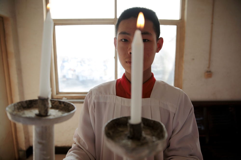 An altar boy holds a candle in preparation for the Palm Sunday procession held by a government-sanctioned Catholic church in Youtong village, Hebei province, China, March 25, 2018. Reuters/Damir Sagolj 